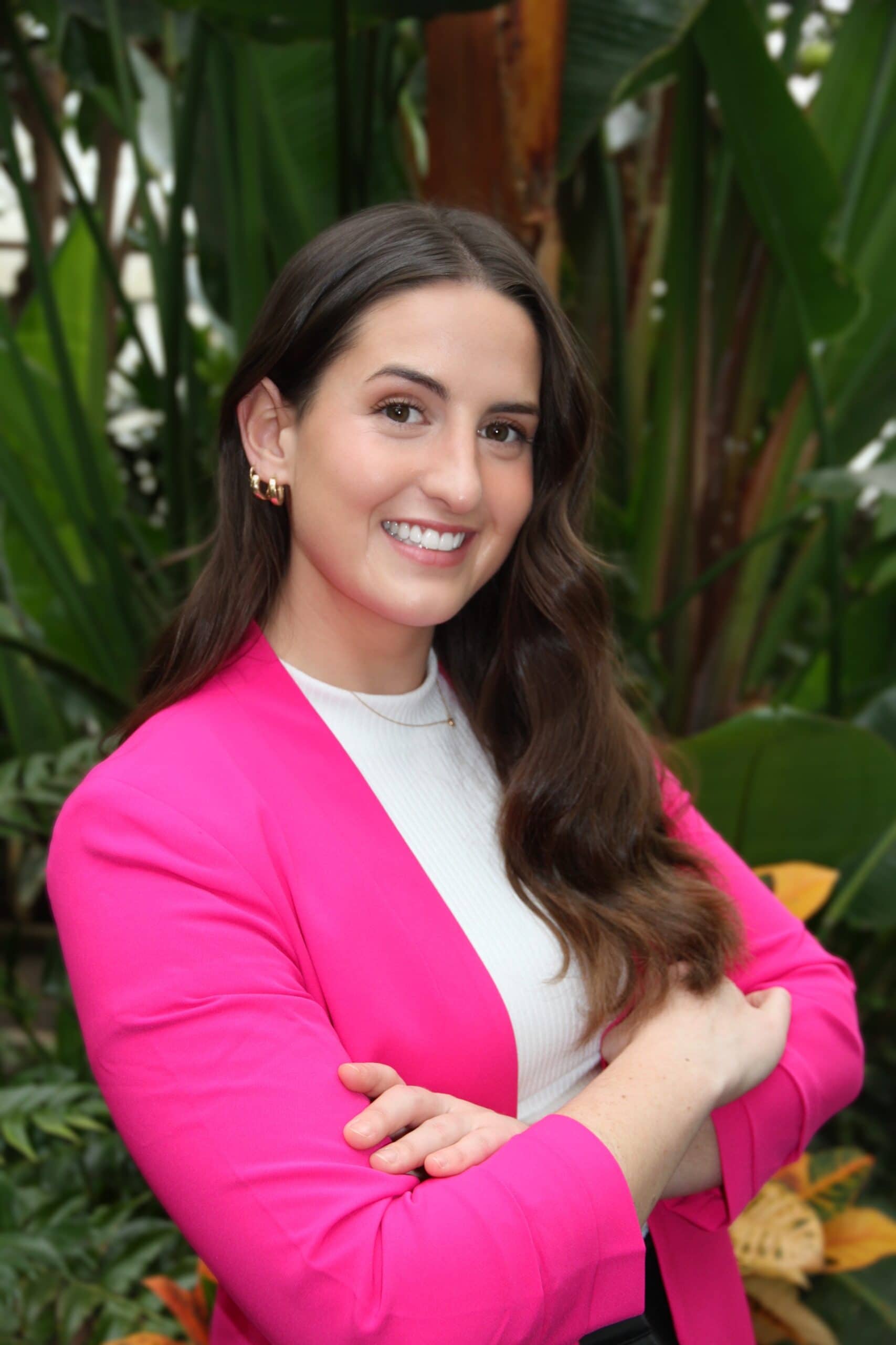 Sarah Herst, a researcher, stands with arms crossed in a pink jacket in front of trees